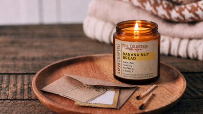 Banana Nut Bread 7oz scented soy blend candle by Lovecrafted, lit in an amber jar on a wooden tray - Fall Collection with banana, walnut, nutmeg and vanilla notes