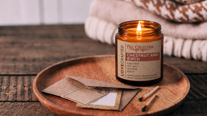 Chestnut and Birch 7oz scented soy blend candle by Lovecrafted, lit in an amber jar on a wooden tray - Fall Collection with chestnut, sea salt, leather and birch notes