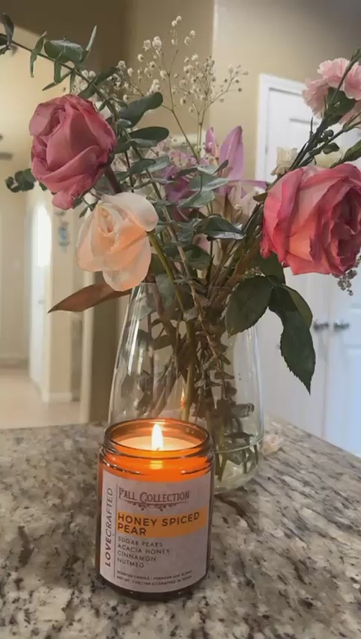 Video of a lit Honey Spiced Pear candle beside a vase of pink roses