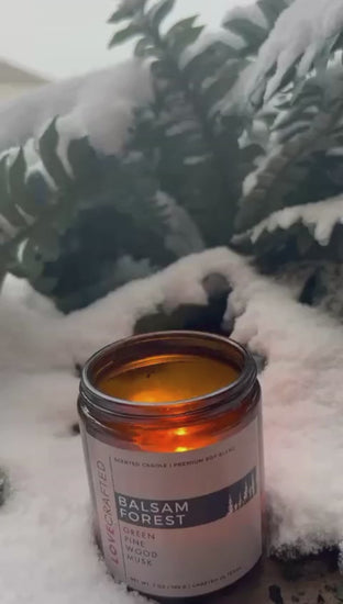 Video of a lit Balsam Forest candle nestled in snow with evergreen branches