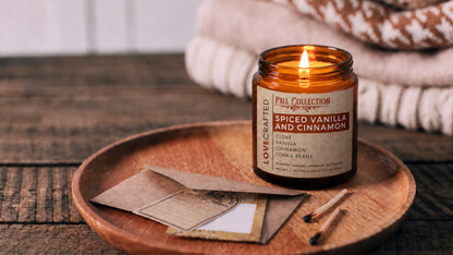 Spiced Vanilla and Cinnamon 7oz scented soy blend candle by Lovecrafted, lit in an amber jar on a wooden tray - Fall Collection with clove, vanilla, cinnamon and tonka bean notes